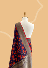 Brown Floral Tussar Georgette Benarasi Saree. Handwoven by skilled weavers at Roliana, this saree features vibrant flowers in fiery red and orange, making it a true statement piece. With a bold red blouse included, this saree is perfect for any special occasion. Shop the best collection of authentic, handwoven, pure benarasi sarees with Roliana New Delhi