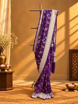 A stunning royal purple saree adorned with delicate multicolour floral and vine motifs, beautifully complemented by a broad silver zari border featuring intricate traditional weaving.