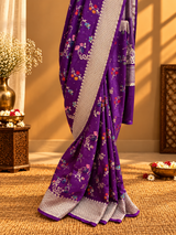 A stunning royal purple saree adorned with delicate multicolour floral and vine motifs, beautifully complemented by a broad silver zari border featuring intricate traditional weaving.