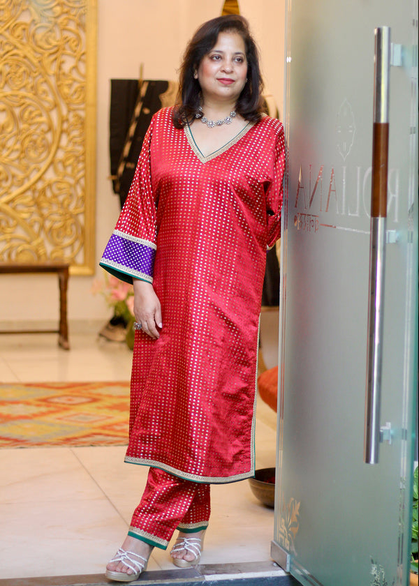 A satin booti choga Co-ordset in crimson red with a vivacious contrast purple sleeve border and gota piping and a coordinated pant in the same fabric and edging. By House of Roliana.