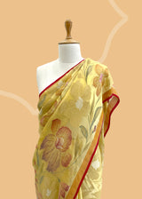 A lemon yellow khaddi Georgette saree with upada floral bootas all over which have detailed hand painted patterns all over and a contrast red kanni . Shop the best collection of authentic, handwoven, pure benarasi sarees with Roliana New Delhi