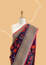 Brown Floral Tussar Georgette Benarasi Saree. Handwoven by skilled weavers at Roliana, this saree features vibrant flowers in fiery red and orange, making it a true statement piece. With a bold red blouse included, this saree is perfect for any special occasion. Shop the best collection of authentic, handwoven, pure benarasi sarees with Roliana New Delhi