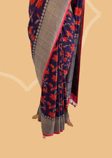 Brown Floral Tussar Georgette Benarasi Saree. Handwoven by skilled weavers at Roliana, this saree features vibrant flowers in fiery red and orange, making it a true statement piece. With a bold red blouse included, this saree is perfect for any special occasion. Shop the best collection of authentic, handwoven, pure benarasi sarees with Roliana New Delhi