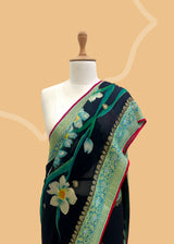 A beautiful Georgette weave saree with zari bootis and border and hand painted in vibrant bunches of pink flowers and green leaves with delicate sky blue lilies in between . A pure Banarasi wedding Sari Shop the best collection of authentic, handwoven, pure benarasi sarees with Roliana New Delhi