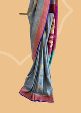 Grey saree with silver gold jaal of floral meenakari, offset with a wine border and pallu, and finished with a bright blue kanni. Shop the best collection of authentic, handwoven, pure benarasi sarees with Roliana New Delhi