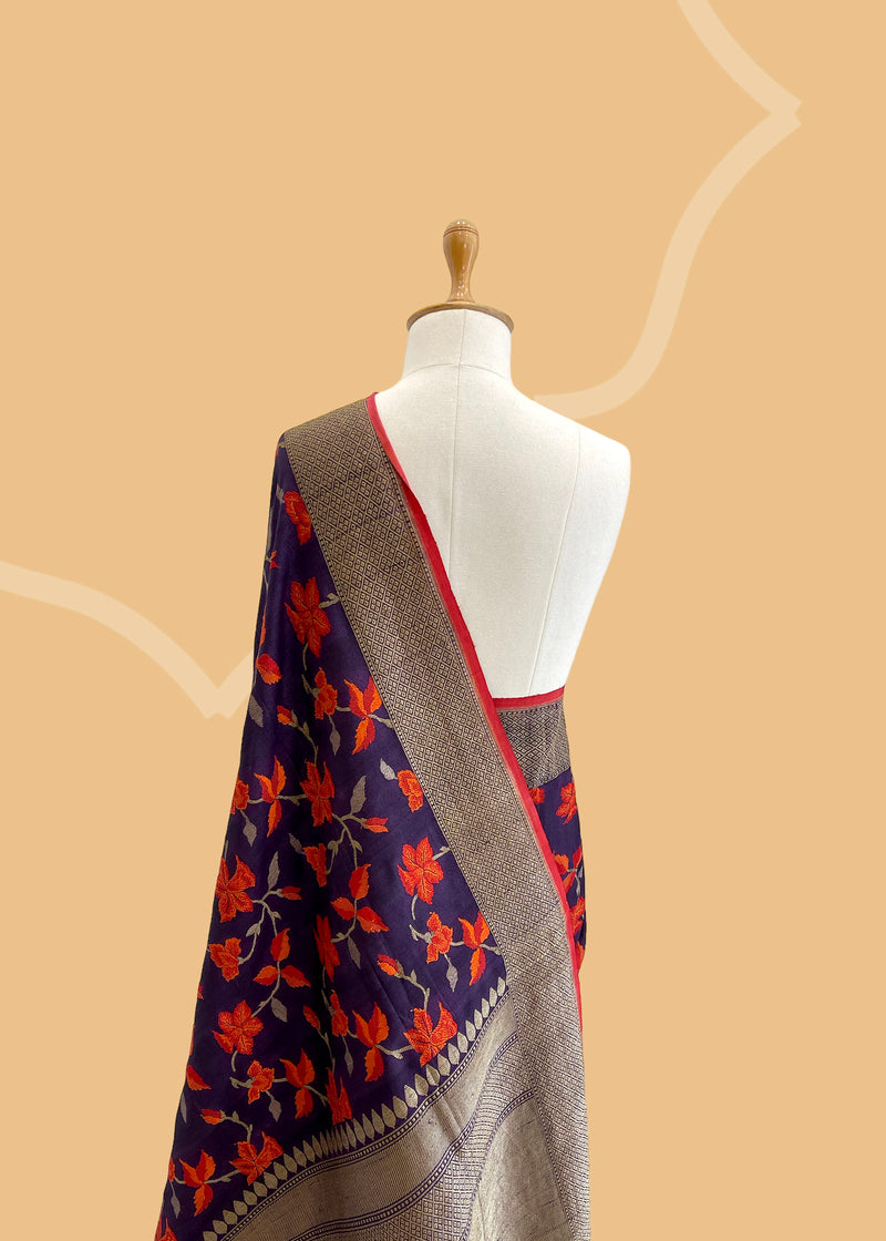 Brown Floral Tussar Georgette Benarasi Saree. Handwoven by skilled weavers at Roliana, this saree features vibrant flowers in fiery red and orange, making it a true statement piece. With a bold red blouse included, this saree is perfect for any special occasion. Shop the best collection of authentic, handwoven, pure benarasi sarees with Roliana New Delhi
