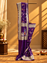 A stunning royal purple saree adorned with delicate multicolour floral and vine motifs, beautifully complemented by a broad silver zari border featuring intricate traditional weaving.
