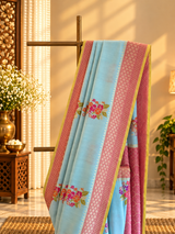 A fresh powder blue muga georgette saree with meenakari floral bootas dismissed off with a pink border and a fresh lime green kanni