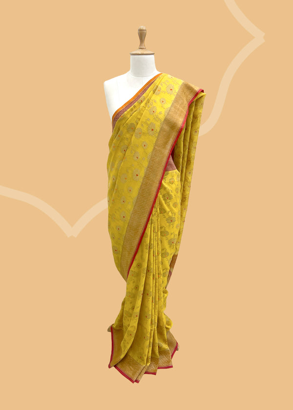 This handwoven, pure tussar georgette saree in a soft yellow hue is adorned with intricate peony bootas and delicate red detailing. Shop the best collection of authentic, handwoven, pure benarasi sarees with Roliana New Delhi