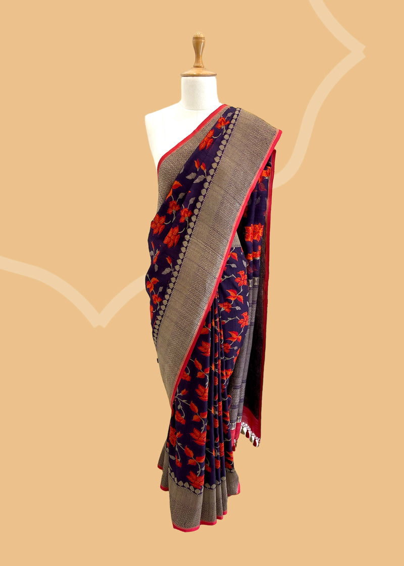 Brown Floral Tussar Georgette Benarasi Saree. Handwoven by skilled weavers at Roliana, this saree features vibrant flowers in fiery red and orange, making it a true statement piece. With a bold red blouse included, this saree is perfect for any special occasion. Shop the best collection of authentic, handwoven, pure benarasi sarees with Roliana New Delhi
