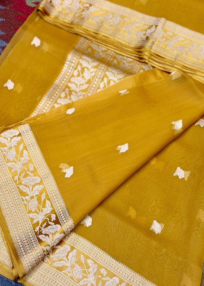 Ochre yellow organza saree boasts delicate woven zari bootis and a satin double woven border perfect for summer wedddings. Shop the best collection of authentic, handwoven, pure benarasi sarees with Roliana New Delhi