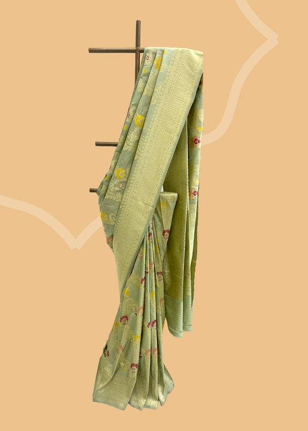This exquisite Benarasi saree from Roliana is crafted from pure Katan Silk. With a sage green oriental jaal kadhwa design and contrast meenakari work, this saree is sure to make an eye-catching statement. An antique old-gold zari weave finishes the elegant look.