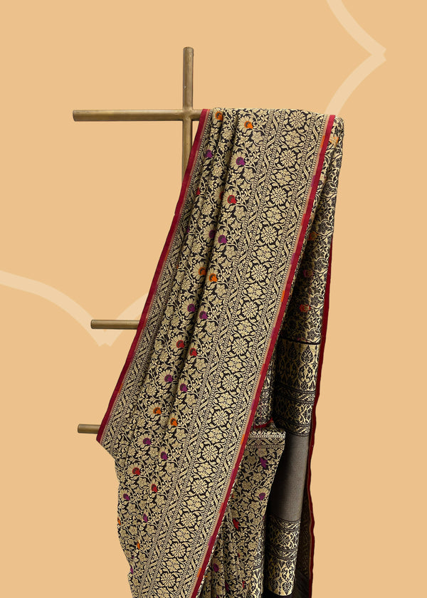  Black Meenakari Pure Silk Benarasi Saree is crafted with a timeless meenakari brocade jaal in dull gold zari with highlights of maroon burnt orange and Rani pink, and a contrast red kanni. It is intricately handwoven by Roliana artisans,