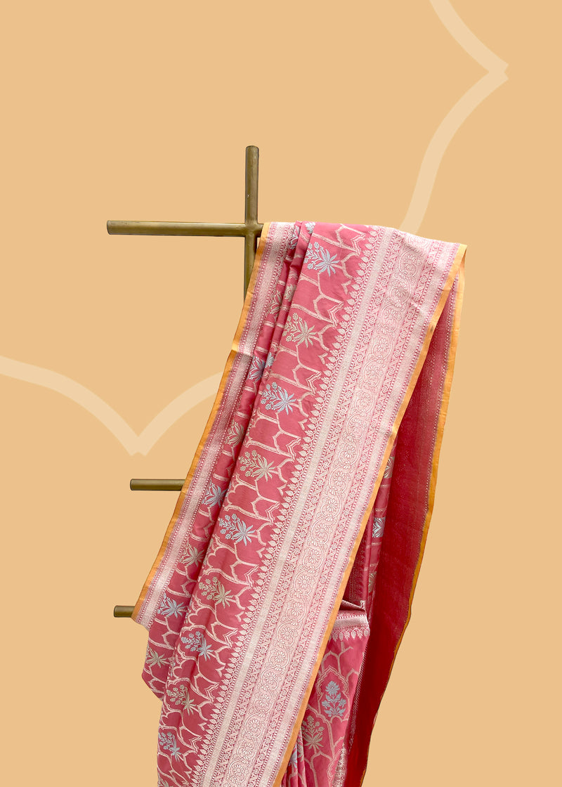 This exquisite saree features an elegant ektaara design in a beautiful salmon pink shade, embellished with powder blue and sage green motifs in an oriental jaal pattern. Shop the best collection of authentic, handwoven, pure benarasi sarees with Roliana New Delhi
