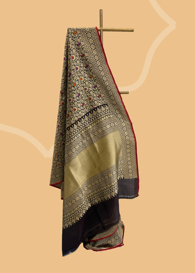  Black Meenakari Pure Silk Benarasi Saree is crafted with a timeless meenakari brocade jaal in dull gold zari with highlights of maroon burnt orange and Rani pink, and a contrast red kanni. It is intricately handwoven by Roliana artisans,