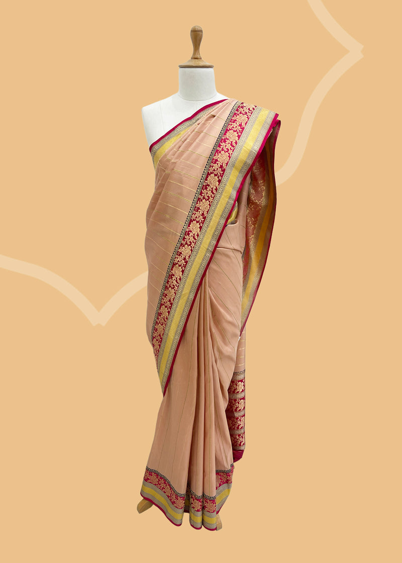 A soft peach gajji saree with vertical stripes in zari complemented by a Rani pink floral woven border and another golden yellow border for that extra special look. Shop the best collection of authentic, handwoven, pure benarasi sarees with Roliana New Delhi
