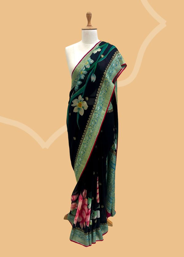 A beautiful Georgette weave saree with zari bootis and border and hand painted in vibrant bunches of pink flowers and green leaves with delicate sky blue lilies in between . A pure Banarasi wedding Sari Shop the best collection of authentic, handwoven, pure benarasi sarees with Roliana New Delhi