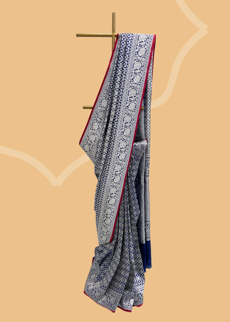 An ink blue silk saree in silk brocade with a silver zari jaal and a contrast red kanni  pure Banarasi sari. Shop the best collection of authentic, handwoven, pure benarasi sarees with Roliana New Delhi