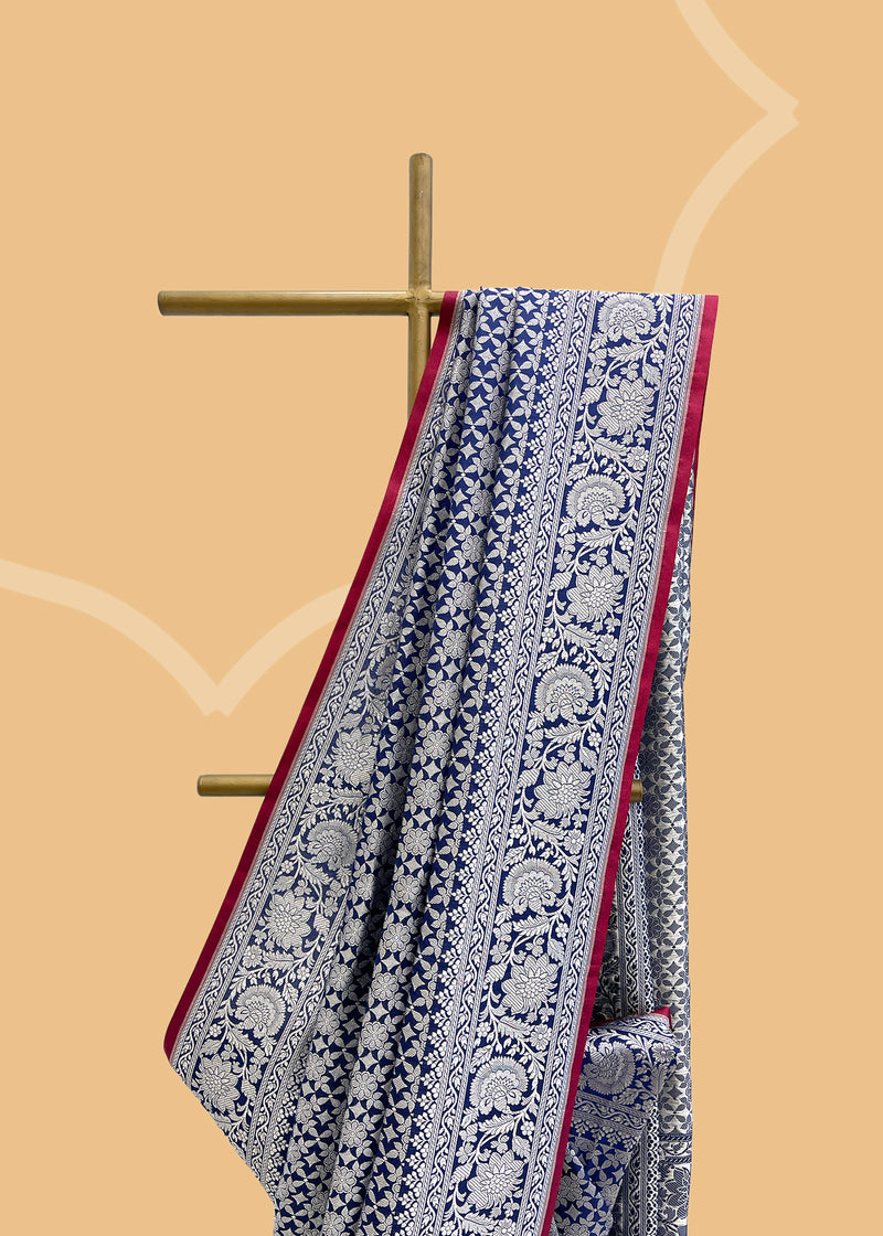 An ink blue silk saree in silk brocade with a silver zari jaal and a contrast red kanni  pure Banarasi sari. Shop the best collection of authentic, handwoven, pure benarasi sarees with Roliana New Delhi