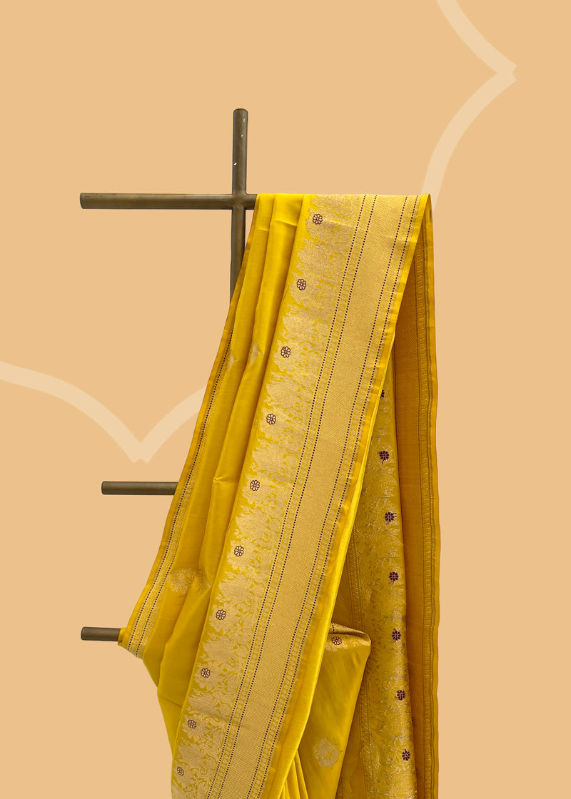 A mustard yellow saree with delicate woven flowers and border in contrast meenakari colours. A pure Banarasi Sari Shop the best collection of authentic, handwoven, pure benarasi sarees with Roliana New Delhi