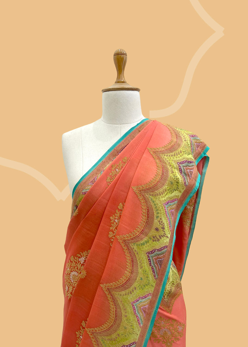 A salmon peach saree in Georgette fabric with a detailed scallop border hand-painted in defferent shades of green,pink firozi with zari ornament bootas and a firozi kanni. A pure Banarasi wedding Sari Shop the best collection of authentic, handwoven, pure benarasi sarees with Roliana New Delhi