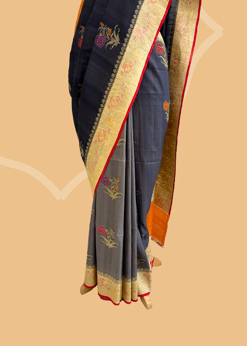 A charcoal black to gray shaded tussar Georgette saree with meenakari bootis and a floral self border and pallu . A pure Banarasi wedding Sari Shop the best collection of authentic, handwoven, pure benarasi sarees with Roliana New Delhi