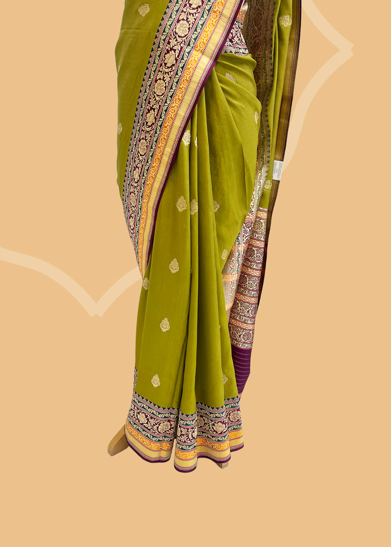 An olive green gajji silk saree with delicate bootis all over and a beautiful contrasting border with jewel toned colours of purple emerald and ochre shades. Shop the best collection of authentic, handwoven, pure benarasi sarees with Roliana New Delhi