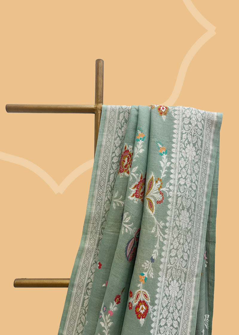 Sage green tussar georgette saree with a colourful meenakari jaal and silver zari bootis and border. Shop the best collection of authentic, handwoven, pure benarasi sarees with Roliana New Delhi