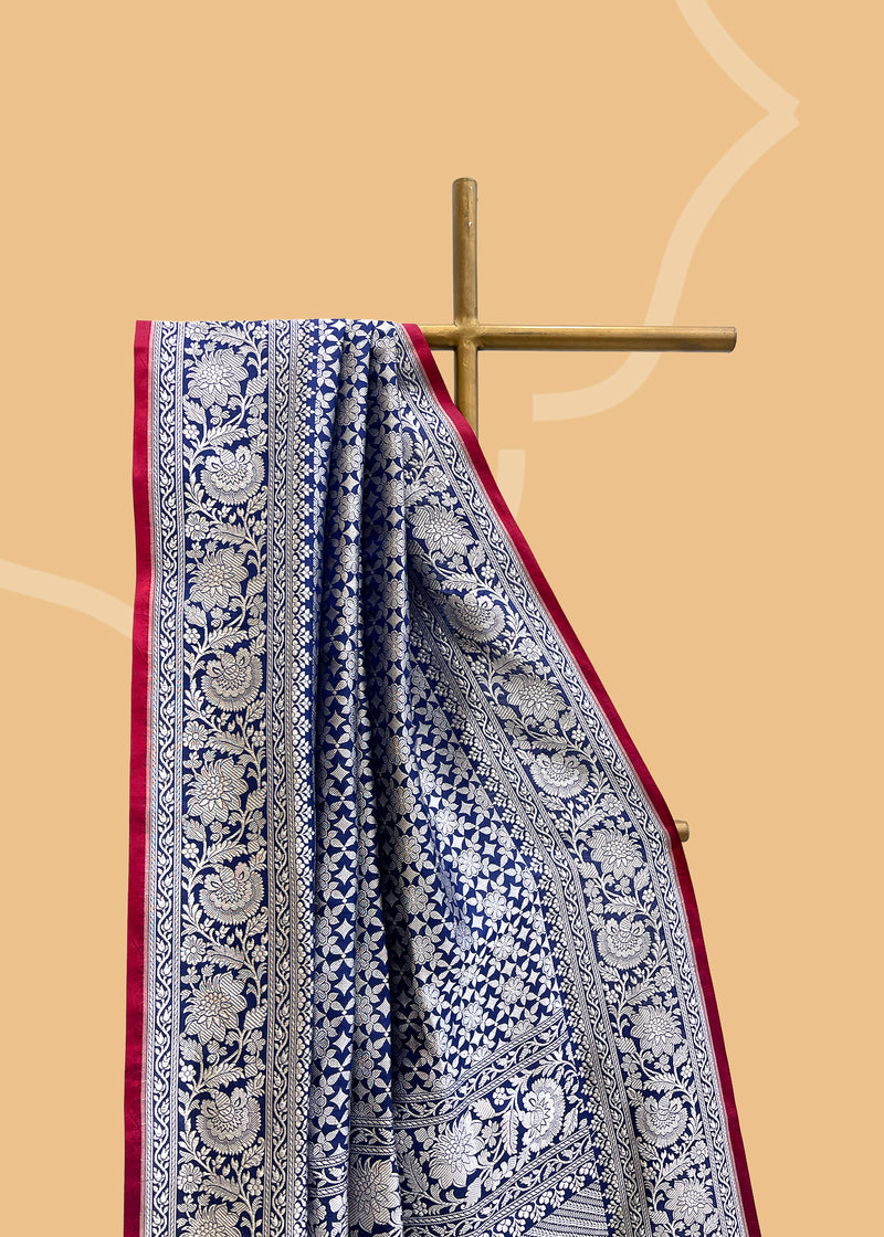 An ink blue silk saree in silk brocade with a silver zari jaal and a contrast red kanni  pure Banarasi sari. Shop the best collection of authentic, handwoven, pure benarasi sarees with Roliana New Delhi