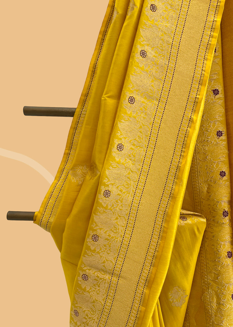 A mustard yellow saree with delicate woven flowers and border in contrast meenakari colours. A pure Banarasi Sari Shop the best collection of authentic, handwoven, pure benarasi sarees with Roliana New Delhi