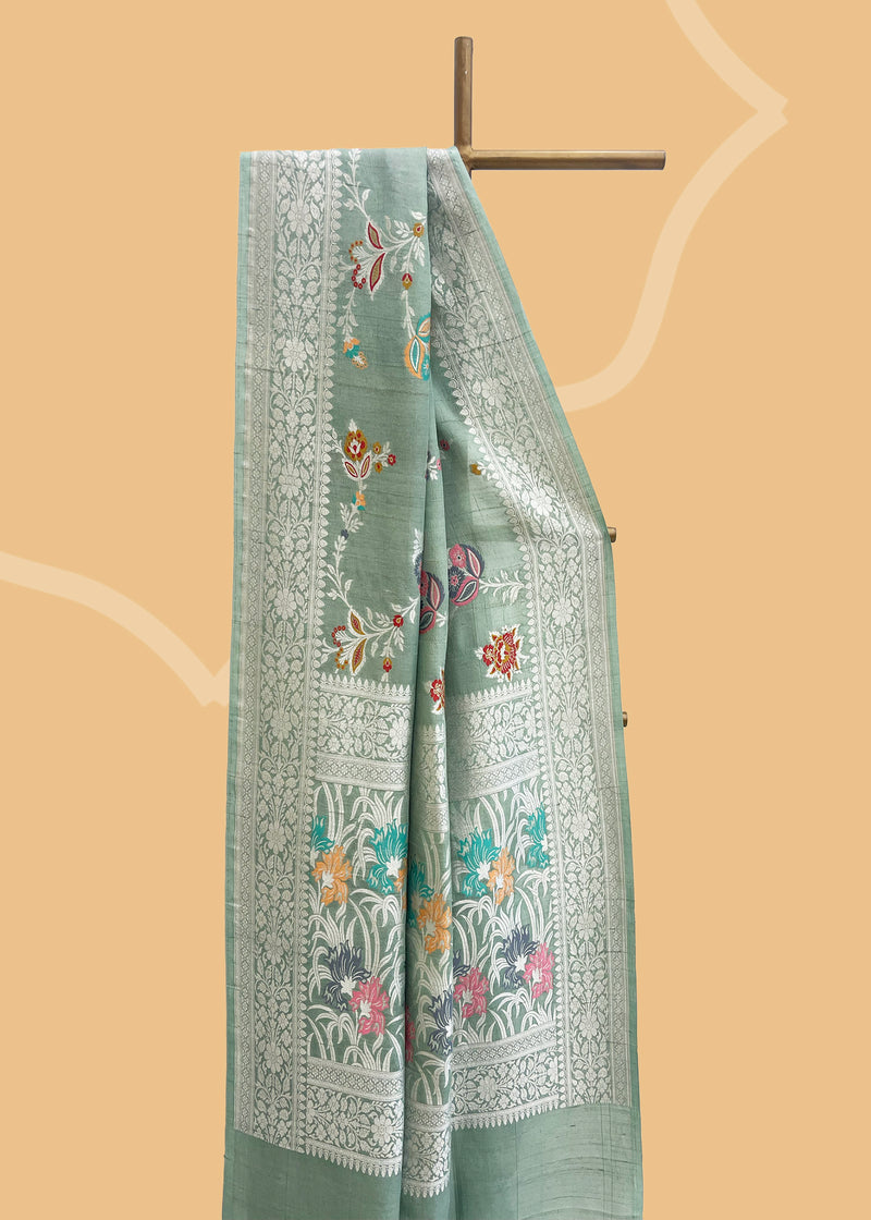 Sage green tussar georgette saree with a colourful meenakari jaal and silver zari bootis and border. Shop the best collection of authentic, handwoven, pure benarasi sarees with Roliana New Delhi